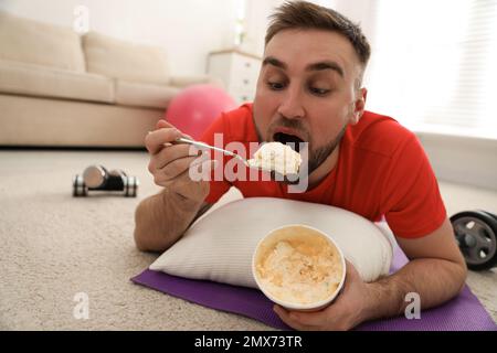 Fauler junger Mann, der Eis isst, anstatt zu Hause zu trainieren Stockfoto