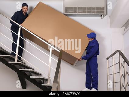 Professionelle Arbeiter, die Kühlschränke auf Treppen in Gebäuden tragen Stockfoto