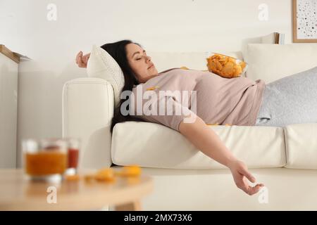 Faule, übergewichtige Frau mit Chips, die zu Hause auf dem Sofa ruht Stockfoto