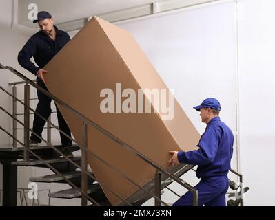 Professionelle Arbeiter, die Kühlschränke auf Treppen in Gebäuden tragen Stockfoto