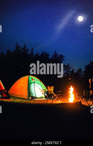 Leuchtendes Zelt in der Nähe von Lagerfeuer in der Wildnis in der Nacht Stockfoto