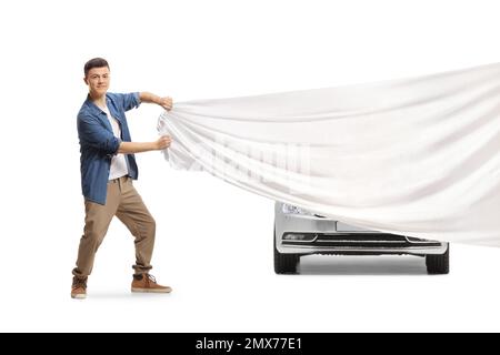 Ein langes Porträt eines jungen, lässigen Mannes, der ein Auto versteckt, mit einem großen weißen Stoff isoliert auf weißem Hintergrund Stockfoto