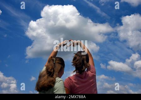 Zwei Schwestern, Mädchen im Teenageralter, bilden gemeinsam ein Herz. Sie drücken ihre Liebe für die Natur und den Himmel aus, für den Himmel oder für jeden anderen Stockfoto