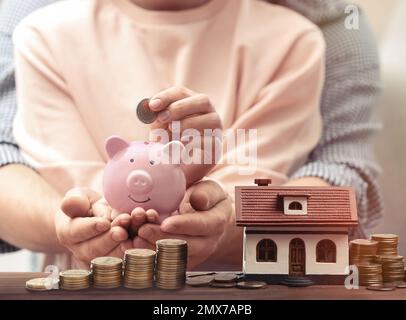 Ein Paar, das Geld in Sparschwein für zukünftigen Hauskauf steckt, Schließung Stockfoto