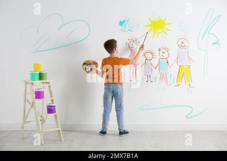 Ein kleines Kind, das eine Familie auf einer weißen Wand drinnen zeichnet Stockfoto