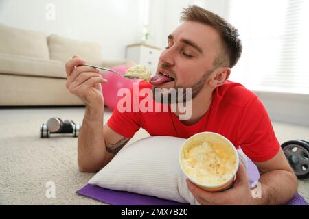 Fauler junger Mann, der Eis isst, anstatt zu Hause zu trainieren Stockfoto