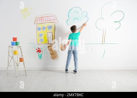 Ein kleines Kind, das Wolken auf weiße Wände drinnen zeichnet Stockfoto