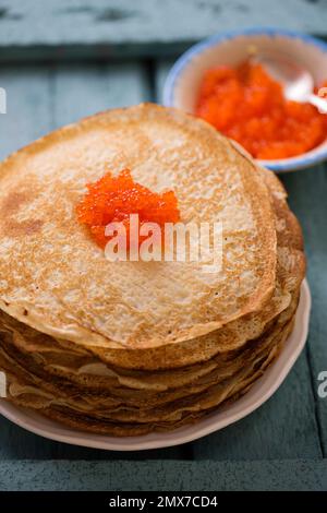 Köstliche dünne, rohe Pfannkuchen auf einem Teller mit rotem Kaviar auf Holzhintergrund Stockfoto