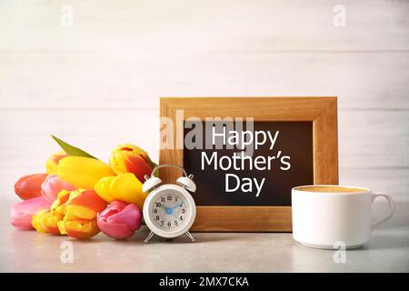 Tafel mit Satz HAPPY MOTHER's DAY, Tulpen, Tasse Kaffee und Wecker auf Lichttisch Stockfoto