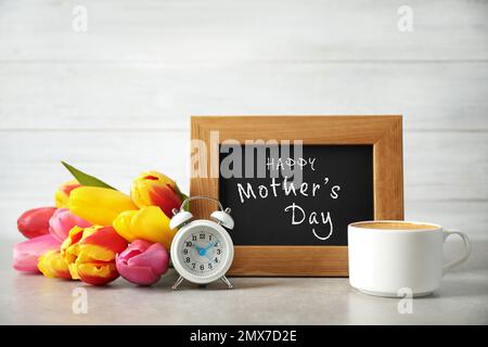 Tafel mit Satz HAPPY MOTHER's DAY, Tulpen, Tasse Kaffee und Wecker auf Lichttisch Stockfoto