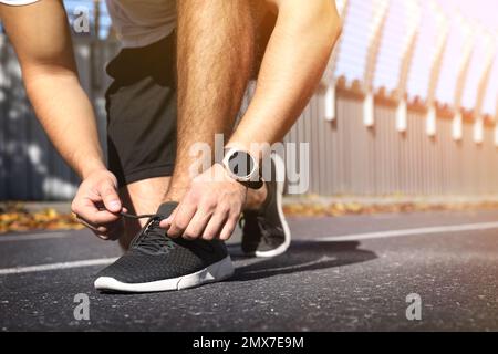 Sportlicher Mann, der an sonnigen Tagen im Stadion Schnürsenkel bindet. Nahaufnahme Stockfoto