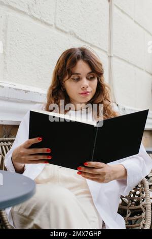 Buch für das Magazin „Mockup Image“. Das Mädchen am Tisch des Cafés, das Buch liest. Stockfoto
