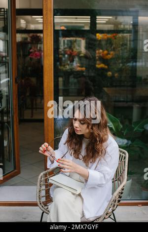 Bildmodell eines Magazins oder Buches. Ein junges Hipstermädchen liest eine Zeitschrift vor dem Hintergrund eines gemütlichen Cafés. Stockfoto