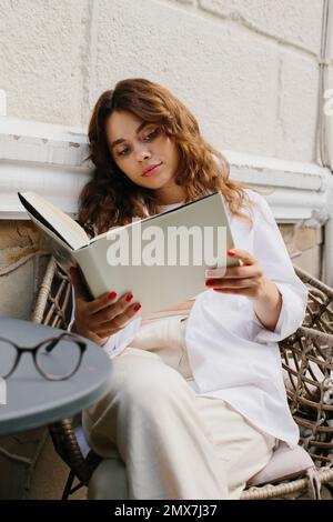 Buch für das Magazin „Mockup Image“. Das Mädchen am Tisch des Cafés, das Magazin liest. Stockfoto