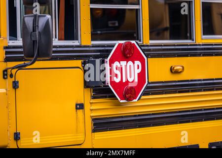 Nahaufnahme eines gelb-orangefarbenen Schulbusses mit einem roten Stoppschild für die Rückkehr zur Schule Stockfoto