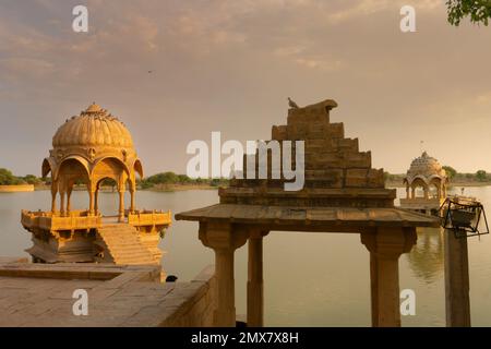 Chhatris und Schreine der hinduistischen Götter und Göttinnen am Gadisar-See, Jaisalmer, Rajasthan, Indien. Indo-islamische Architektur, Sonnenuntergang und bunte Wolken Stockfoto