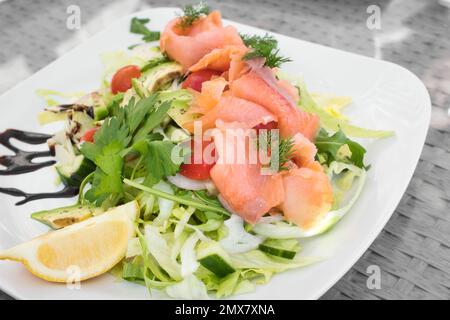 Geräucherter Lachs und Avocadosalat mit grünem Salat, Dill, Kirschtomaten und Gurke, mit einer Scheibe Zitrone Stockfoto