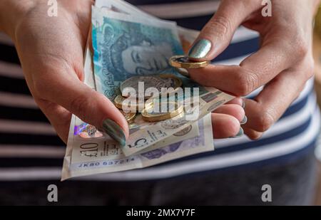 Nahaufnahme der Hände einer Frau mit Bargeld , mit Banknoten und Münzen verschiedener Stückelungen der britischen Währung . Stockfoto