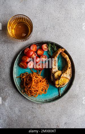 Blick von oben auf das Lachssteak mit scharfen Karotten und Kirschtomaten, serviert mit einem Glas trockenen Weißwein auf Beton Stockfoto