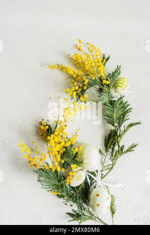 Osterkarte mit leuchtend gelben Mimosablüten und einem Nest voller Eier auf weißem Hintergrund Stockfoto