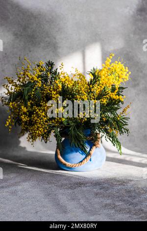 Vase mit Frühlingsgelben Mimosablüten an sonnigen Tagen auf einem Steintisch Stockfoto