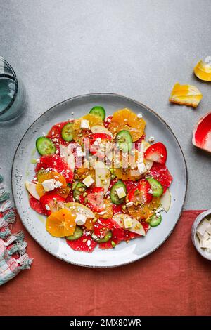 Top View von gesundem Salat mit Orangen und Erdbeeren und Äpfeln und Gurken serviert mit Käse und Nüssen auf dem Teller Stockfoto