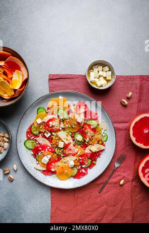 Top View von gesundem Salat mit Orangen und Erdbeeren und Äpfeln und Gurken serviert mit Käse und Pistazien auf dem Teller Stockfoto