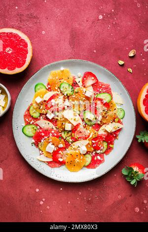 Top View von gesundem Salat mit Orangen und Erdbeeren und Äpfeln und Gurken serviert mit Käse und Pistazien auf dem Teller Stockfoto