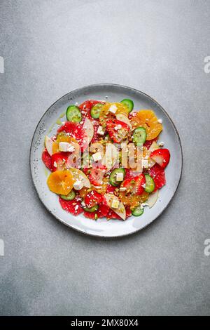 Top View von gesundem Salat mit Orangen und Erdbeeren und Äpfeln und Gurken serviert mit Käse und Pistazien auf dem Teller Stockfoto