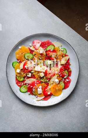 Top View von gesundem Salat mit Orangen und Erdbeeren und Äpfeln und Gurken serviert mit Käse und Pistazien auf dem Teller Stockfoto