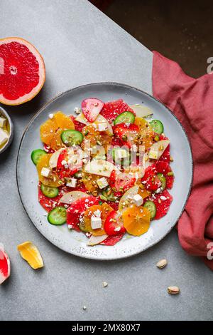 Top View von gesundem Salat mit Orangen und Erdbeeren und Äpfeln und Gurken serviert mit Käse und Pistazien auf dem Teller Stockfoto