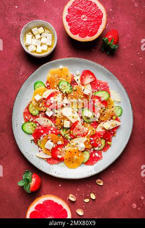 Top View von gesundem Salat mit Orangen und Erdbeeren und Äpfeln und Gurken serviert mit Käse und Pistazien auf dem Teller Stockfoto