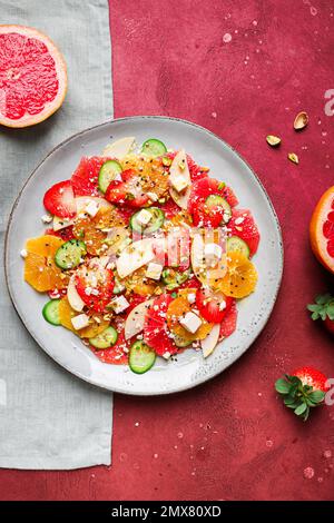 Top View von gesundem Salat mit Orangen und Erdbeeren und Äpfeln und Gurken serviert mit Käse und Pistazien auf dem Teller Stockfoto