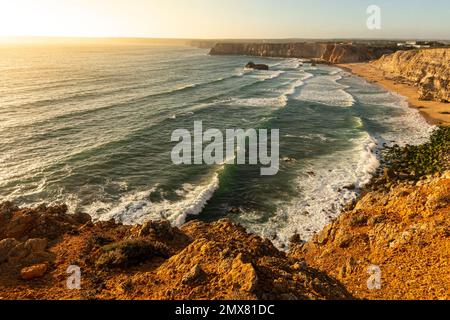 Luftaufnahme des endlosen Meeres mit schaumigen Wellen an der felsigen Küste und Sandstrand bei windigem Wetter bei Sonnenuntergang Stockfoto