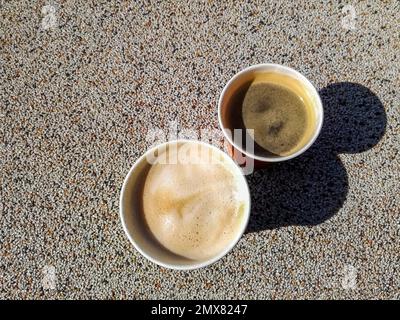 Zwei tragbare Einweg-Pappbecher in verschiedenen Größen mit kaffeehaltigen Schatten auf rauer Oberfläche. Draufsicht. Kaffee Zum Mitnehmen. Nahaufnahme. Selektiver Fokus Stockfoto