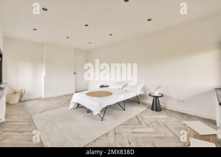 Inneneinrichtung des modernen Schlafzimmers mit minimalistischen Möbeln und Teppich an weißen Wänden und Parkettboden Stockfoto