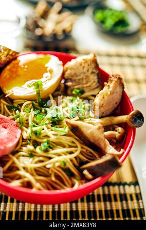 Von oben aus schmackhafte Ramen-Suppe mit Fleisch und Ei und Nudeln, serviert in der Schüssel auf dem Tisch in der Nähe von Essstäbchen und Glasbecher Stockfoto