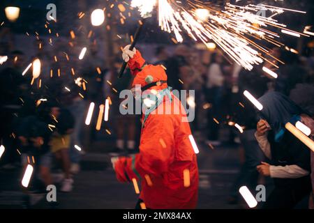 Seitenansicht einer anonymen Person in farbenfrohen Kostümen mit Schutzbrille, die während der Weihnachtsfeier auf überfülltem Stree mit brennenden Funkeln unterwegs ist Stockfoto