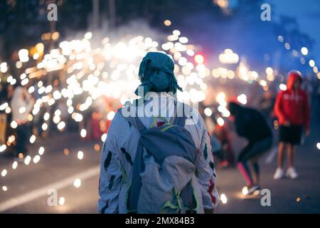 Rückansicht einer nicht wiedererkennbaren Person in Kostüm und Kopftuch mit Rucksack, der auf einer überfüllten Straße mit brennenden Glitzern am Weihnachtstag steht Stockfoto