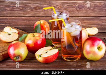 Frischer Apfelsaft aus biologischem Anbau mit Eis im Glas mit rohen ganzen und geschnittenen roten Äpfeln auf holziger Hintergrundfarbe Stockfoto