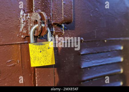 Braune Metalltür mit gelbem Vorhängeschloss verschlossen Stockfoto