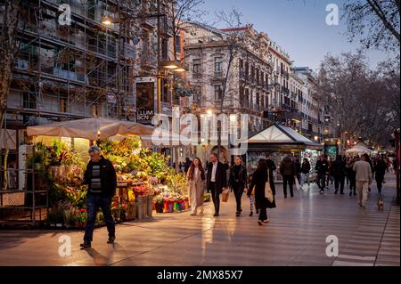 Blumenstände und Kioske sind zu sehen, während die Menschen die La Rambla Avenue in Barcelona in der Dämmerung entlang gehen. Stockfoto