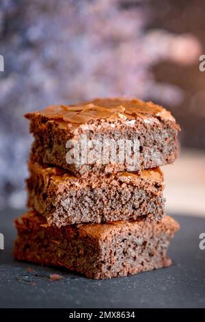 Hausgemachter Brownies-Kuchen mit dunkler Schokolade, gestapelt auf einer Steinplatte mit Kopierbereich. Lavendelblüten im Hintergrund Stockfoto