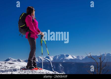 Schneewanderer in den Bergen mit Schneeschuhen, Schneestöcken und Rucksack. Frau mittleren Alters, volle Länge. Stockfoto