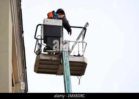 Arbeiter in der hydraulischen Hebebühne reparieren die Gebäudefassade. Baumeister auf Hebebühne in der Nähe des Hauses, Bau- und Reparaturarbeiten Stockfoto