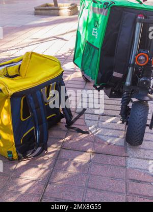 Caceres, Spanien - 19. Januar 2021: Lieferrucksäcke und elektrische Kicker. Urbaner Hintergrund Stockfoto