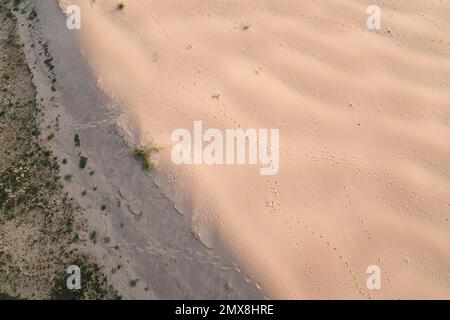 Blick von oben auf Fußabdrücke, die über eine Sanddüne in Südostasien führen. Stockfoto