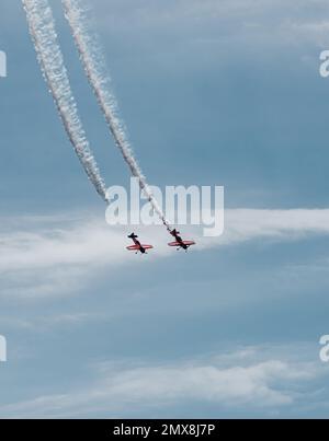 Zwei kleine Flugzeuge fliegen parallel und beschreiben eine weiße Flugbahn über dem blauen Himmel. Kondensationsspuren. Synchronisierung von Konzepten und Zuordnung. Stockfoto