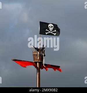 Jolly Roger, Piratenflagge und Krähennest auf einem Mast vor einem bewölkten Himmel. Barry Island. Januar 2023. Im Winter. Stockfoto