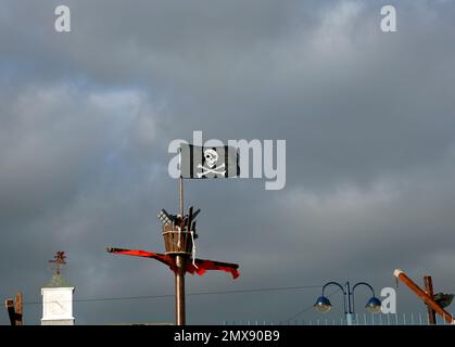 Jolly Roger, Piratenflagge und Krähennest auf einem Mast vor einem bewölkten Himmel. Barry Island. Januar 2023. Im Winter. Stockfoto